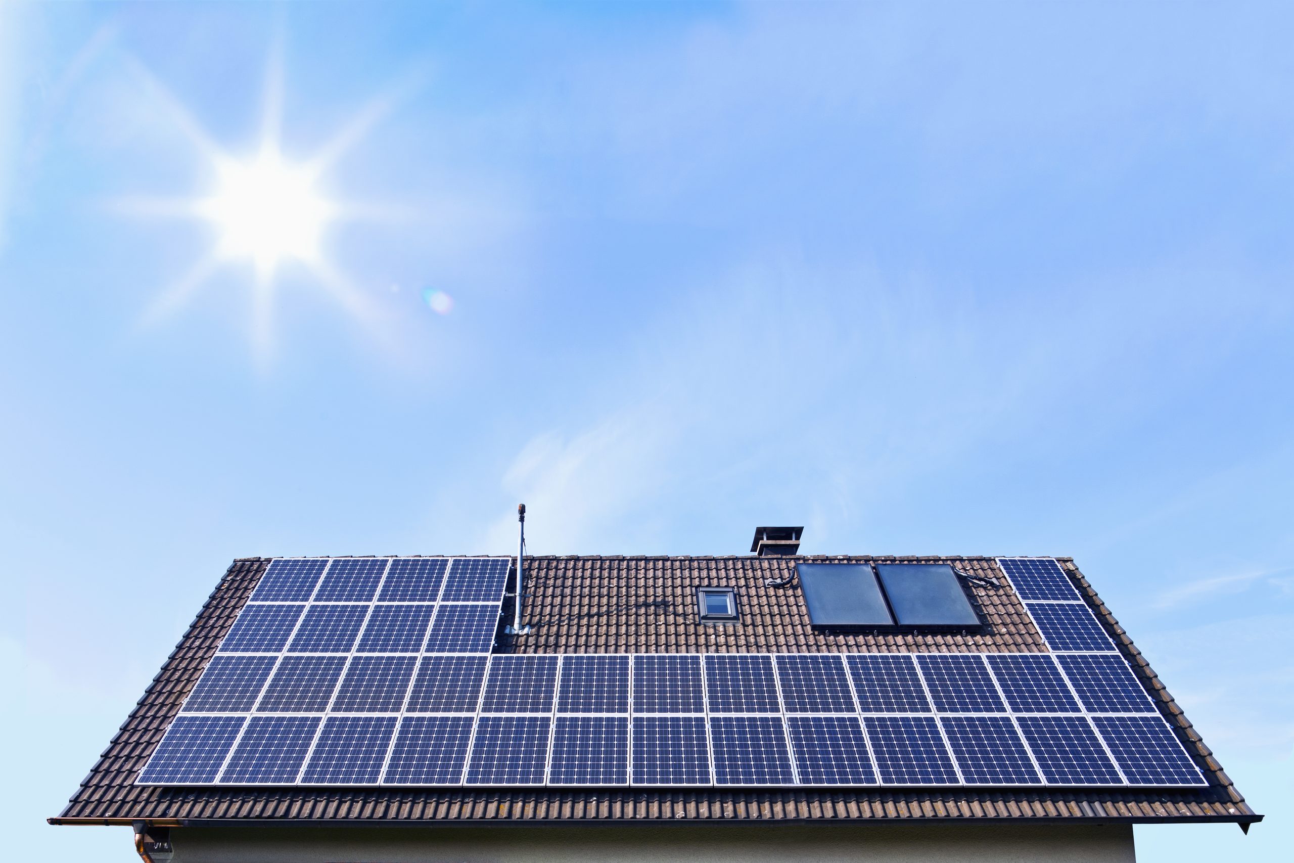 Solar panels on a tiled house roof under a bright sun and blue sky