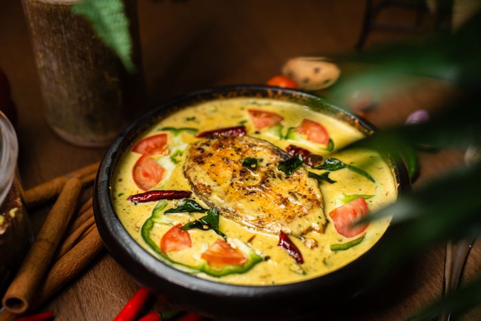 Kerala fish moilee in a black pan, garnished with curry leaves