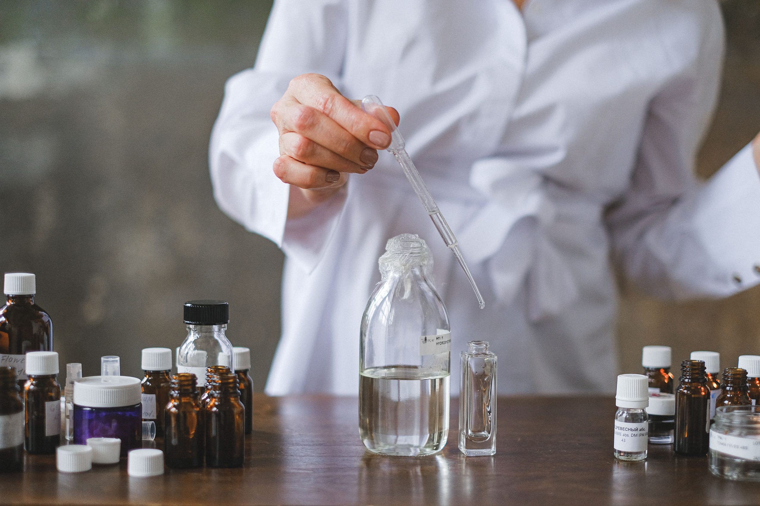 A person in a white coat transferring liquid between glass bottles