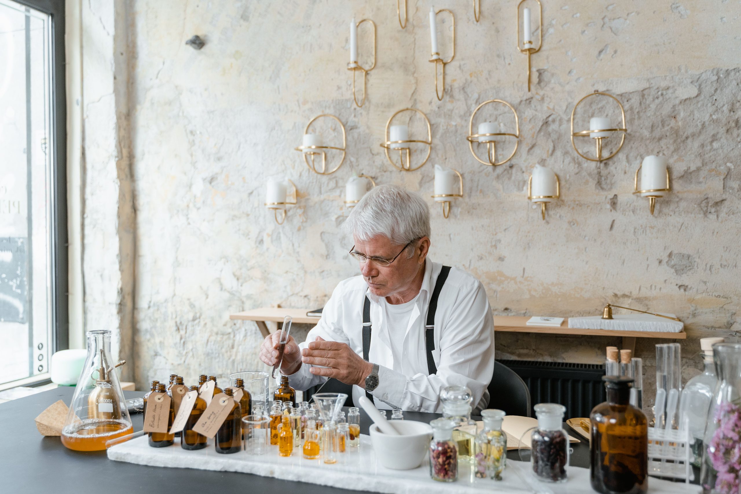 A perfumer at a bench lined with small bottles, working under warm light