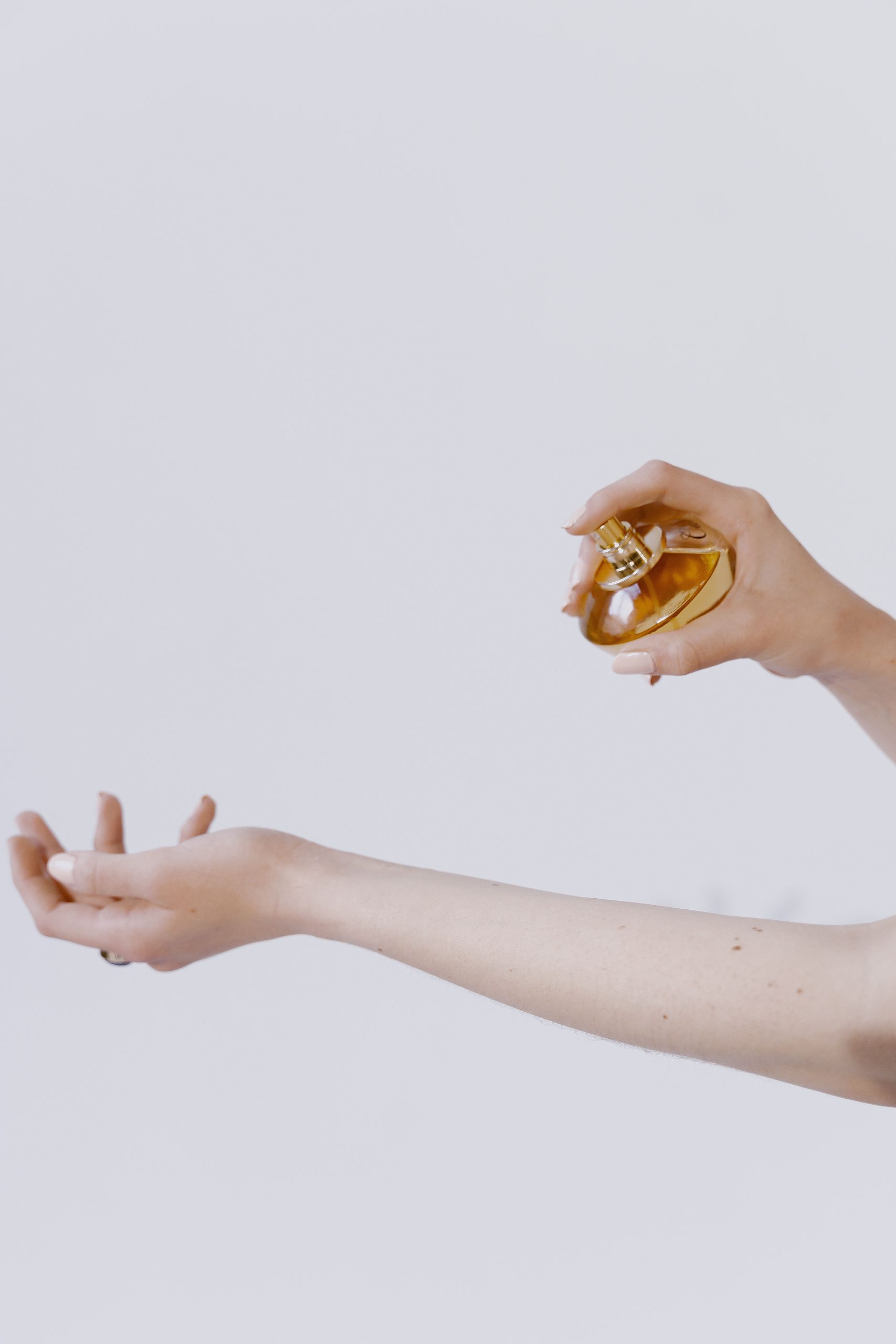 A hand misting fragrance onto a bare wrist against a pale background