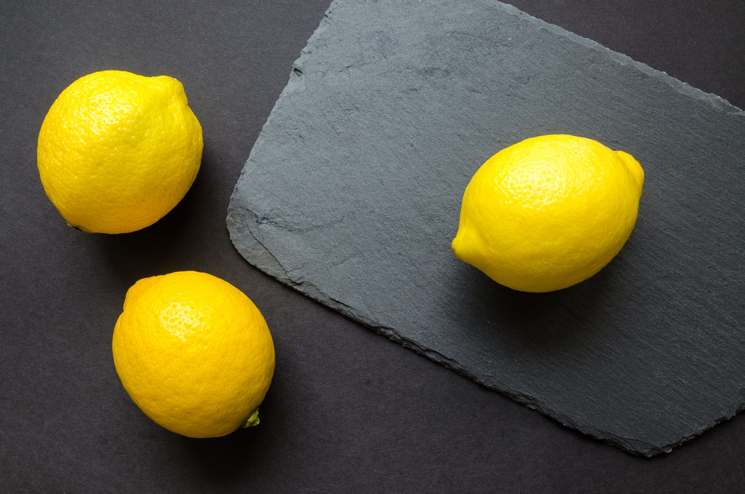 Three yellow citrus fruits on a slate board